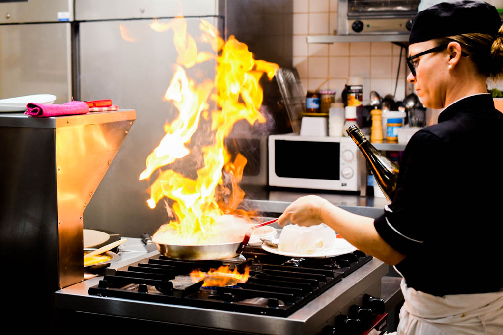 Prestations │ Cuisinière aux fourneaux de son restaurant flambant une crêpe